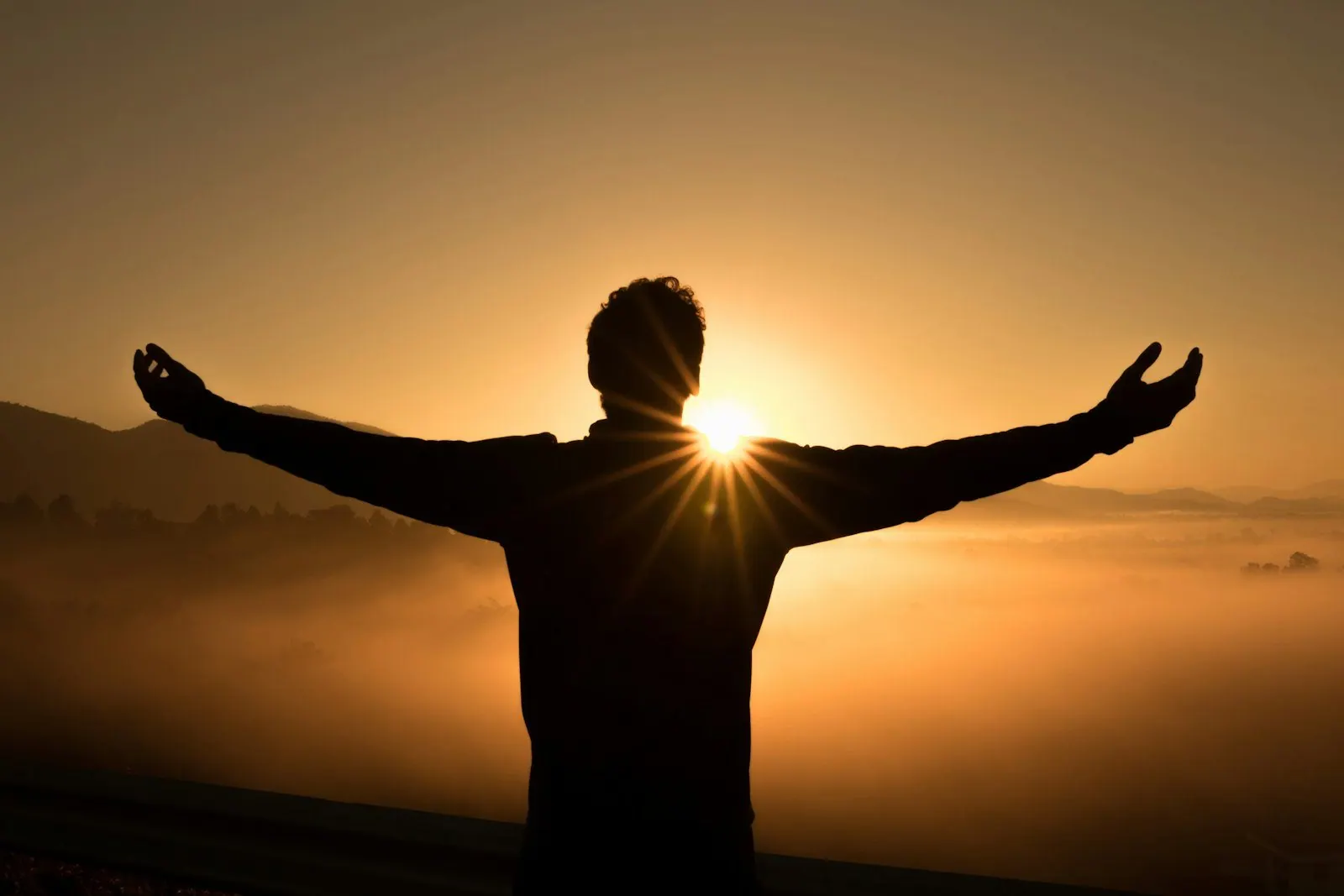 A figure with arms open to a sunrise